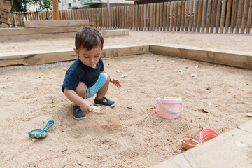 Toddler boy playing sandpit with toy spade
