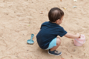 Toddler boy playing with sand in sandbox