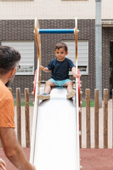 Toddler sitting on playground slide with father