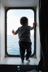 Child looking out ship window at sea