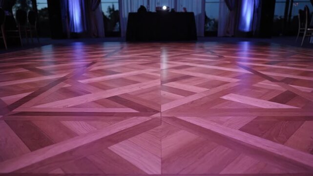Empty wooden dance floor with geometric parquet pattern and purple spotlight. Elegant event venue setup for a university graduation party, prom, or wedding reception