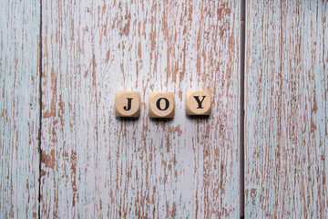 Letter cubes forming the word &ldquo;Joy&rdquo; on a bright wooden background with peeling paint, symbol of happiness and positive energy