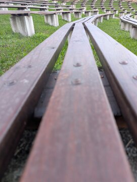 Close-up view of curved wooden benches arranged in rows on a grassy slope, forming part of an outdoor amphitheater. Perspective lines lead the eye through the image, highlighting the rhythmic pattern 