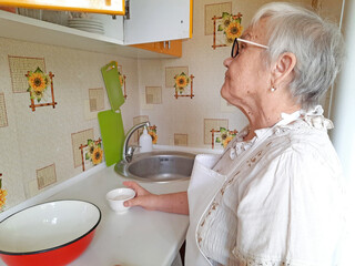 An elderly woman wearing glasses and an apron stands in the kitchen, making pancakes.