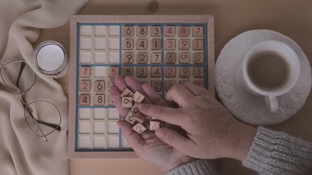 female hands placing number into Sudoku puzzle, solving puzzle on wooden board, Brain exercise, cognitive health, mental agility in mature age