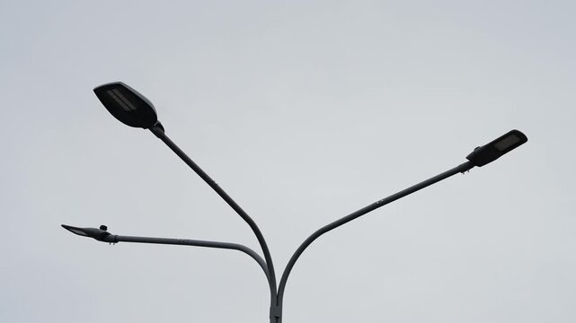 Modern triple-headed streetlight with curved arms rising into an overcast grey sky, capturing minimalist urban infrastructure and symmetrical design along a quiet roadway.