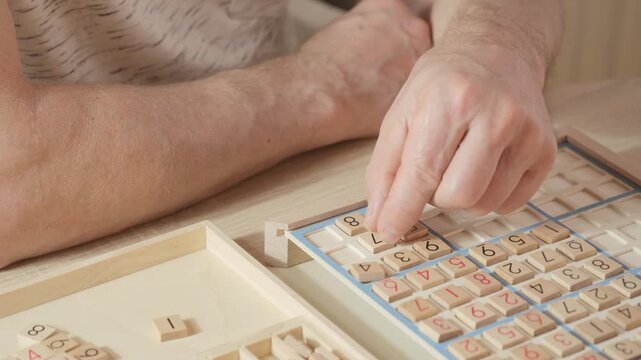 closeup hands carefully placing number into Sudoku puzzle, senior man focused on solving puzzle on wooden board, Brain exercise, cognitive health, and mental agility in mature age, brain health