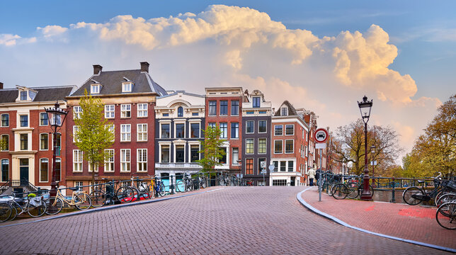 Amsterdam, Netherlands. Bridge with bicycles along road on water canals. Traditional dutch houses with windows on channel banks. Evening urban landscape.