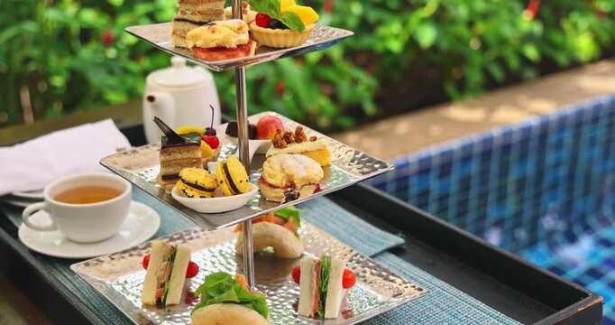 Afternoon tea set sitting by luxury swimming pool at tropical resort, bright sunny lighting, high-end vacation lifestyle.