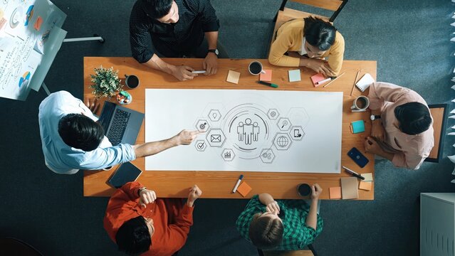 A diverse group of professionals engage in a collaborative meeting at a modern workspace, discussing strategies and ideas with digital elements and creative tools. Raster