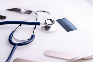 A stethoscope is placed on a scale. The stethoscope is blue and silver. The scale is white