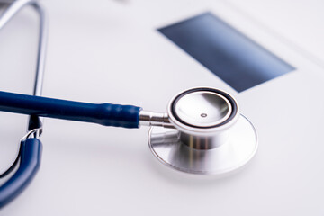 A stethoscope is placed on a white surface. The stethoscope is blue and silver