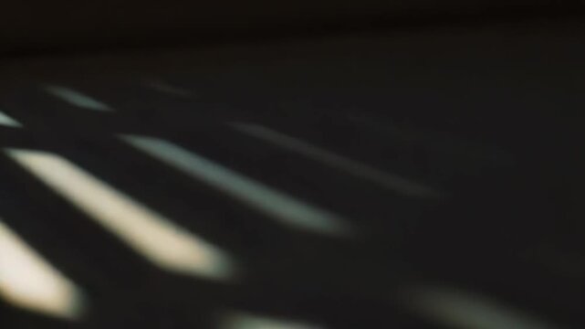 Sunlight filtering through blinds or a narrow opening creating striking parallel lines of light and shadow across a surface, offering an abstract and calm visual mood