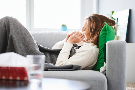 Sick young woman lying on sofa and blowing her nose with a paper tissue