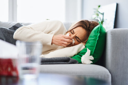 Young woman suffering from flu or cold symptoms lying on couch at home