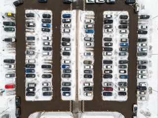 A parking lot with cars in it. The cars are parked in rows and the lot is covered in snow