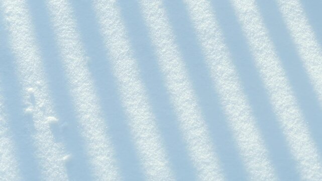 Winter snow surface showing intriguing abstract patterns of diagonal shadow stripes, creating a cool blue and white texture background for seasonal or conceptual designs