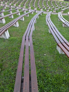 Wide-angle view of multiple rows of curved wooden benches set on a grassy slope, forming a structured amphitheater layout. The repeating forms and perspective lines create a strong visual rhythm. 