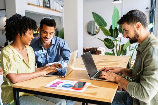Diverse business colleagues working together in modern office. Multicultural professionals collaborating with laptops around a shared table. Teamwork and collaboration concept.