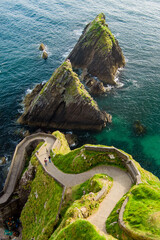 Fototapeta premium Dunquin or Dun Chaoin pier, Ireland's Sheep Highway. Aerial view of narrow pathway winding down to the pier, ocean coastline, cliffs. Popular location on Slea Head Drive and Wild Atlantic Way.