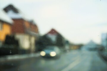 Abstraktes Motiv mit fahrenden Auto mit wei&szlig;en Lichtern auf Hauptstra&szlig;e durch Ortschaft mit H&auml;usern mit roten D&auml;chern bei Frost, Eis und K&auml;lte am Nachmittag im Winter