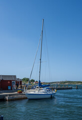 Fototapeta premium Gothenburg, Sweden - June 29 2025: Sailing boat docked beside red wooden huts.