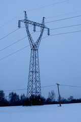 Duży stalowy słup energetyczny na tle zaśnieżonego, zimowego nieba o zmierzchu. Duży  słup  góruje na tle zaśnieżonego, zimowego krajobrazu, otoczony nagimi drzewami. Zmierzch rzuca przyćmione,blaski © Grzegorz
