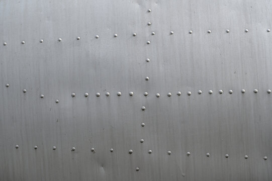 Symmetrical rivet grid on metal surface with matte stripes and repeating fasteners, aircraft skins, rivets on duralumin. Abstract industrial pattern for contemporary design and architectural backdrops
