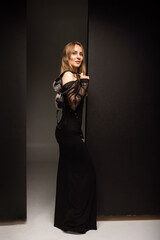 A girl in a black dress stands sideways and holds a bra in her hand.