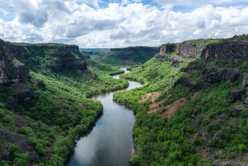 A scenic view of a river winding through lush green cliffs under a partly cloudy sky