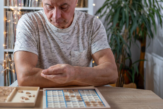 senior man focused on solving sudoku puzzle on wooden board, Brain exercise, cognitive health, and mental agility in mature age, mental stimulation, brain health