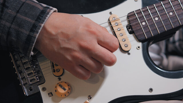 Detailed close-up shot of a musician's hand playing an electric guitar. Focus on the strings, pickups, and fretboard. Conveys a mood of creativity, practice, and passion for music. Neutral colors