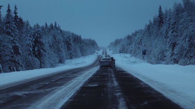 Car is driving on a frozen road in ice. Driver drives a car on a snowy highway in winter. Polar night in Arctic pine forest. Cold weather. Blizzard in winter journey, outdoor. Snowstorm in road trip.