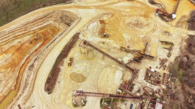Machines operate at a mining site in an undeveloped location. Ground is disturbed with dirt and tools scattered around. This scene shows industrial activity in a natural setting.
