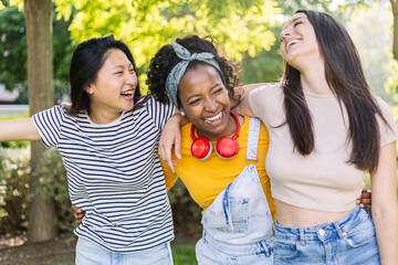 Young group of diverse teenage girls having fun together at city park, laughing while walking...