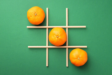 Tic tac toe game made with oranges on green background, flat lay