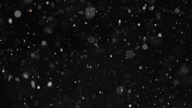 Abstract winter background with falling snow on a black backdrop. Blurred snowflakes, ice particles, and bokeh motion create a cinematic blizzard effect for Christmas, New Year, and seasonal overlays.