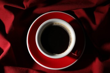 Naklejka premium Cup of aromatic coffee on red fabric, top view