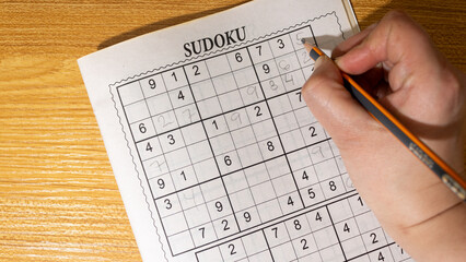 Person playing Sudoku in a small specialized magazine on a wooden background