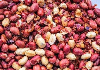 Macro top-down view of a dense pile of roasted peanuts with reddish skins and scattered husks - High-energy protein snack background for health food