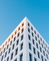 Obraz premium Modern building corner with smooth white facade and geometric window patterns against a clear blue sky, showcasing contemporary architectural design elements