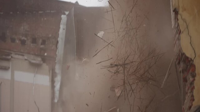 Excavator demolition of an old brick wall, hydraulic claw ripping through masonry and concrete, releasing thick dust clouds and debris as interior fragments and splinters scatter