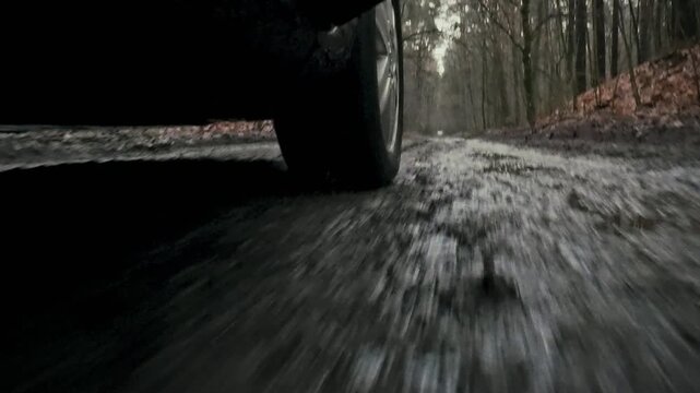 A vehicle's rear wheel spins wildly, kicking up mud puddles on a forest road as it drives through a muddy terrain, demonstrating the wheelbase and axle's motion in a challenging off-road condition