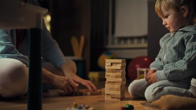 A young daughter and her mother bond over a Jenga game on the floor, constructing a shaky tower with wooden blocks in a warm evening setting, blending playful entertainment and interactive learning