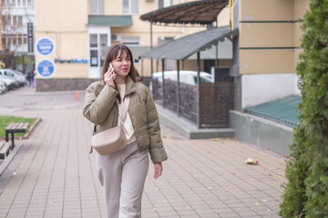 Obraz premium Woman walking on city street while talking on her phone during daytime in urban setting