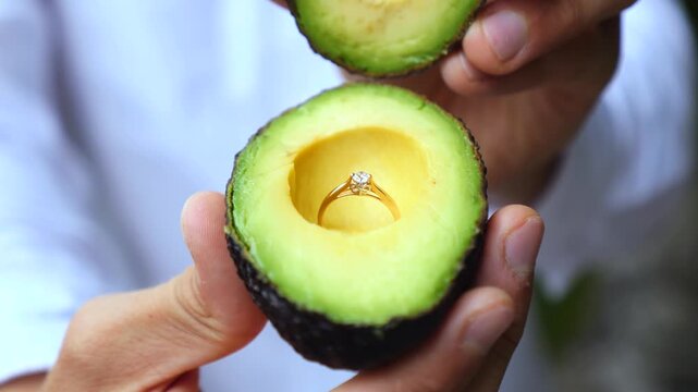 Male hands opening a fresh green avocado to reveal a beautiful diamond engagement ring hidden inside, an original and healthy way to make a creative and surprising marriage proposal
