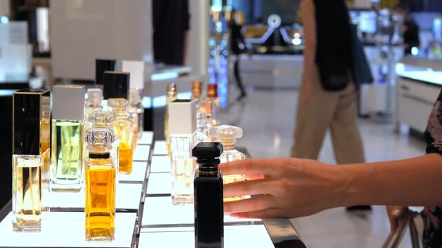 Close up of a female customer's hand selecting a new fragrance from a beautifully lit display shelf in a luxury perfume shop, choosing between various elegant bottles of eau de toilette