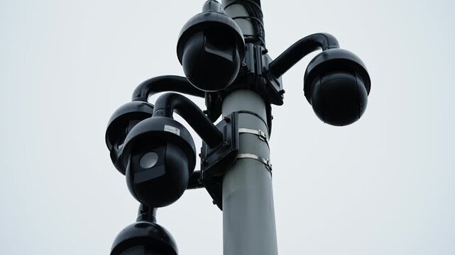 Array of black dome surveillance cameras mounted on a central pole, providing panoramic monitoring beneath an overcast sky, highlighting security infrastructure and observation