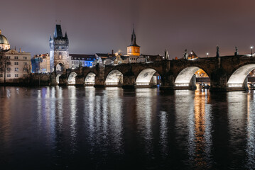 Obraz premium Charles Bridge at Night in Winter Viewed from Lesser Town Riverbank. Vltava River, tourists walking