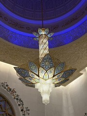 A stunning detailed view of a large and intricate chandelier hanging from a beautifully decorated ceiling inside an opulent mosque